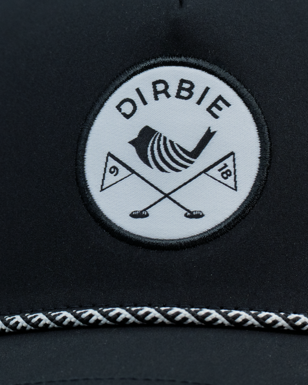 Close-up of a black golf cap featuring a circular white patch with the brand name &